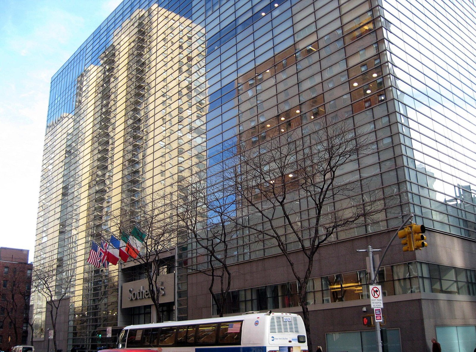 The glass and brick corner of the Sotheby's building on York Avenue in New York, seen from the street with a Sotheby's sign and flags above the entrance