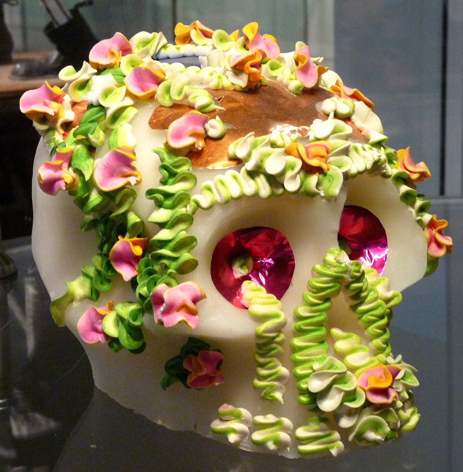 A white sugar skull decorated with green and pink icing flowers and shiny pink foil eyes