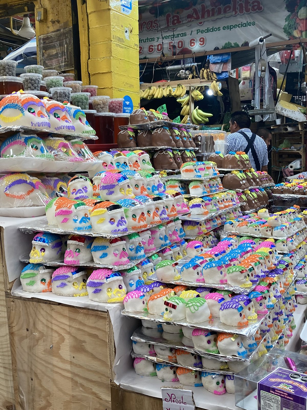 Market stall with shelves of small colorful sugar skulls in rows, with other market goods behind them
