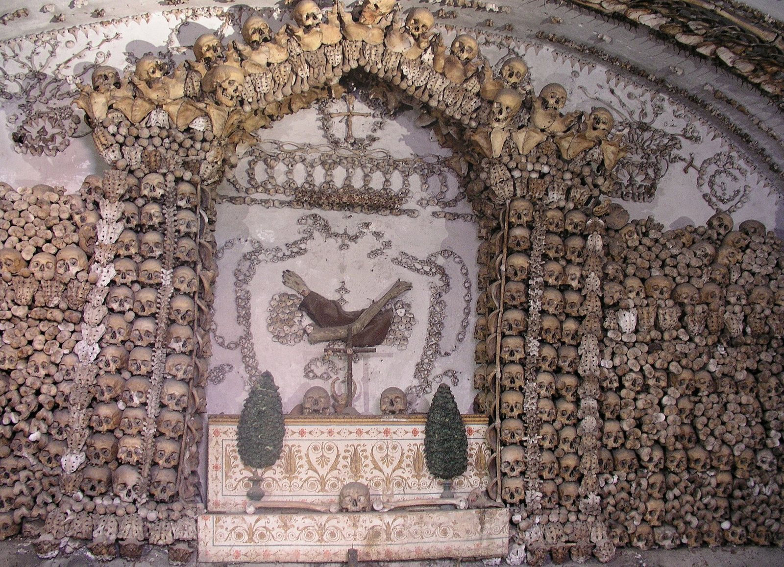 Un nicho de la Cripta de los Capuchinos enmarcado por un arco de cráneos, con muros de cráneos y huesos alrededor y un escudo de huesos sobre un altar
