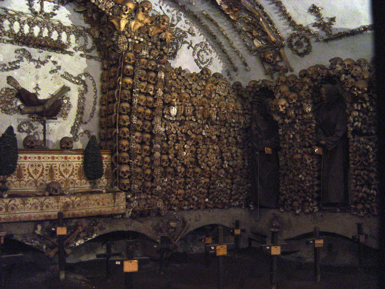 Una capilla de la Cripta de los Capuchinos con un altar a la izquierda y muros de cráneos y huesos, con restos de frailes con hábito en nichos a la derecha