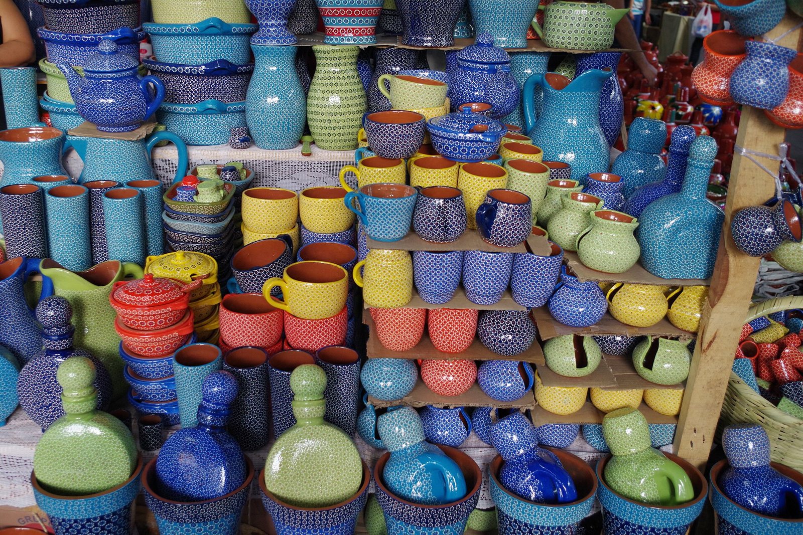 Shelves packed with blue, yellow, green and red glazed pitchers, cups and bottles covered in small dots, the capuleado style of Capula pottery