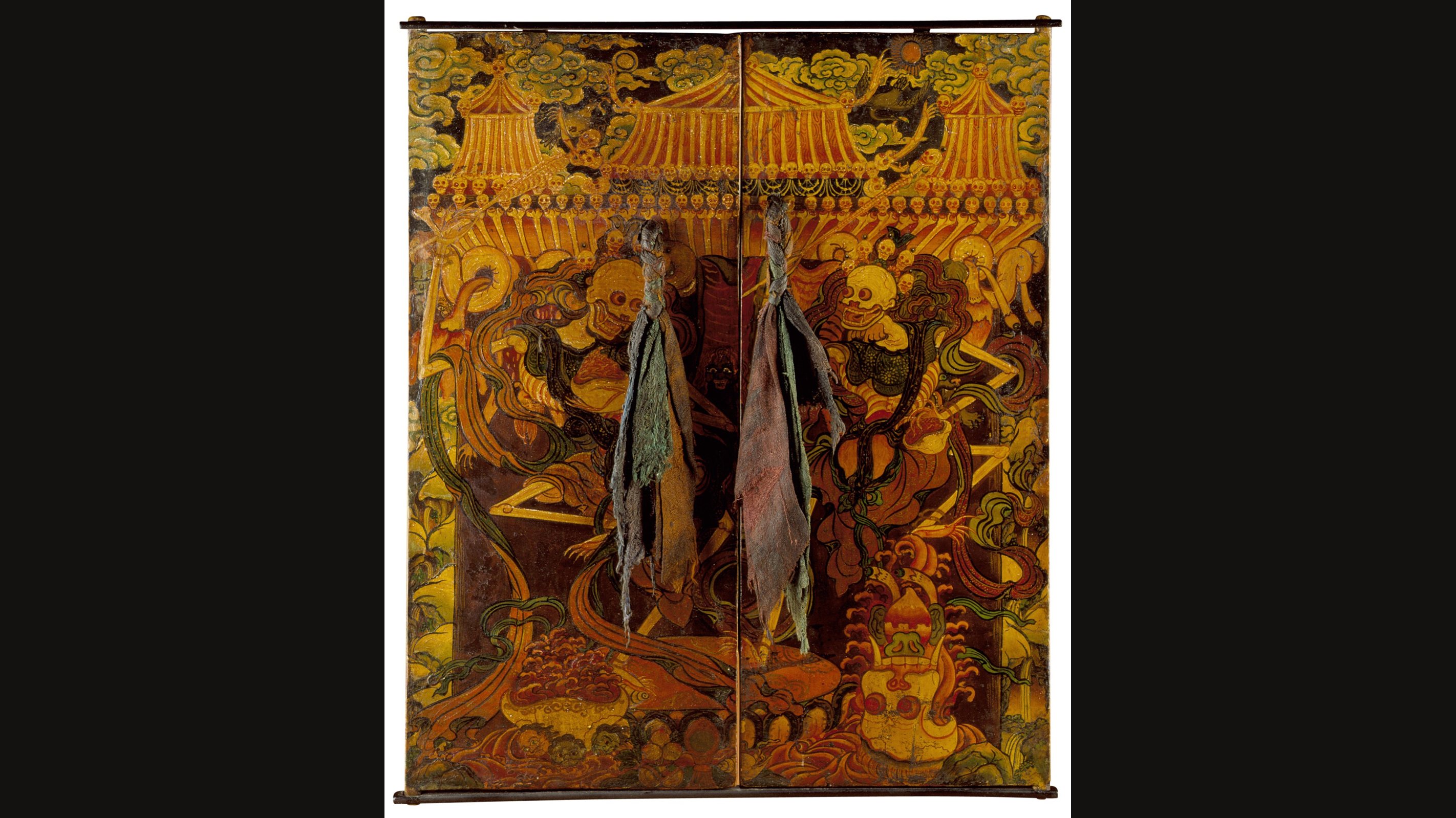 A pair of painted wooden cabinet doors on a golden ground, each showing a dancing skeleton among swirling clouds and flames beneath a row of pavilion roofs, with faded cloth tassels hanging down the centre