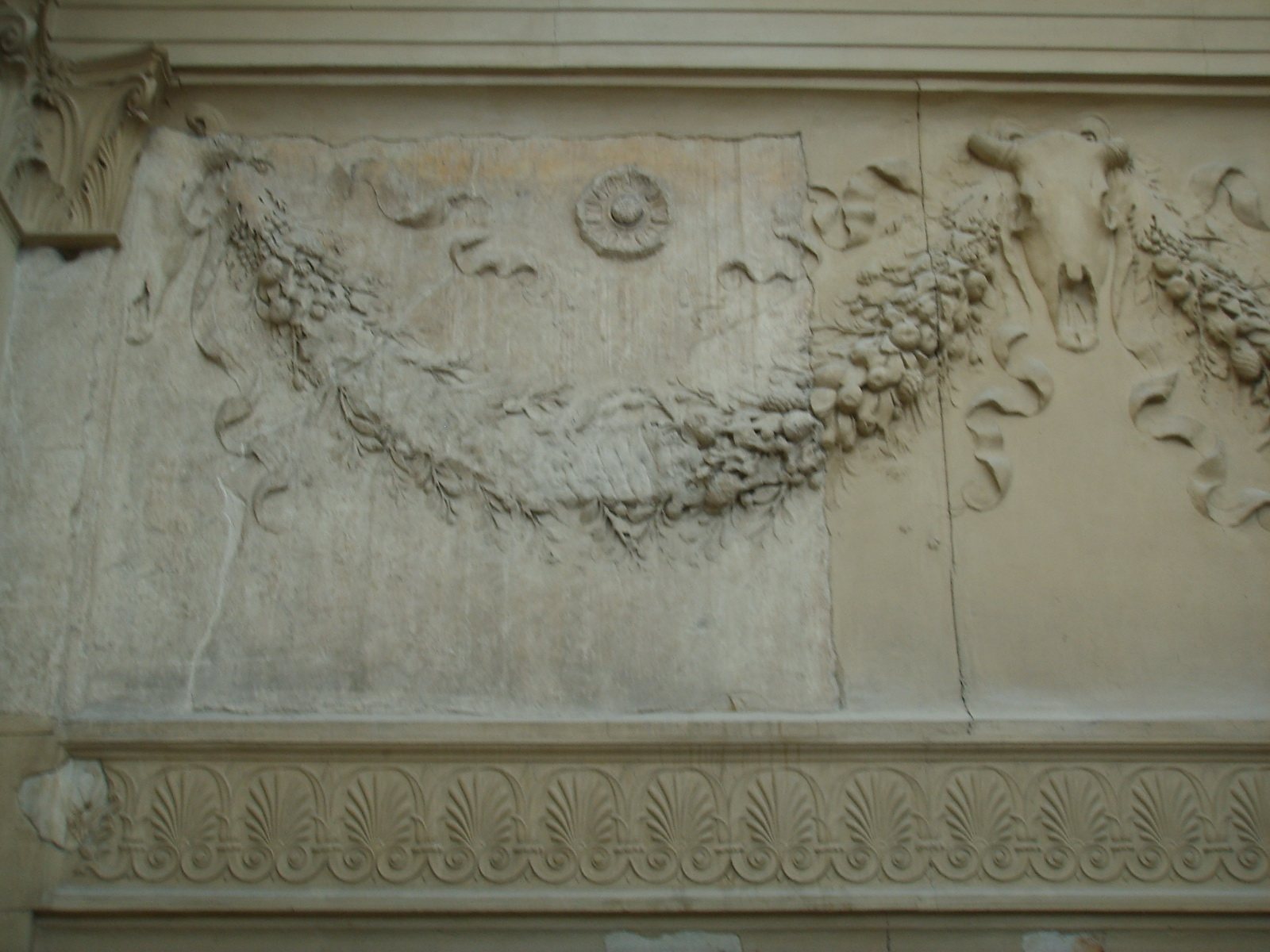 Carved marble wall with a heavy fruit garland, a round rosette and an ox skull hung with ribbons, above a band of palmette ornament