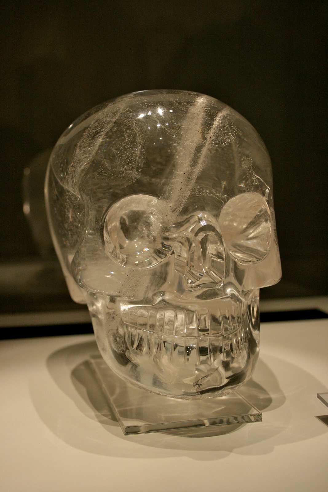 Front view of the British Museum's crystal skull, a clear quartz skull with deep round eye sockets and carved teeth, on a clear stand