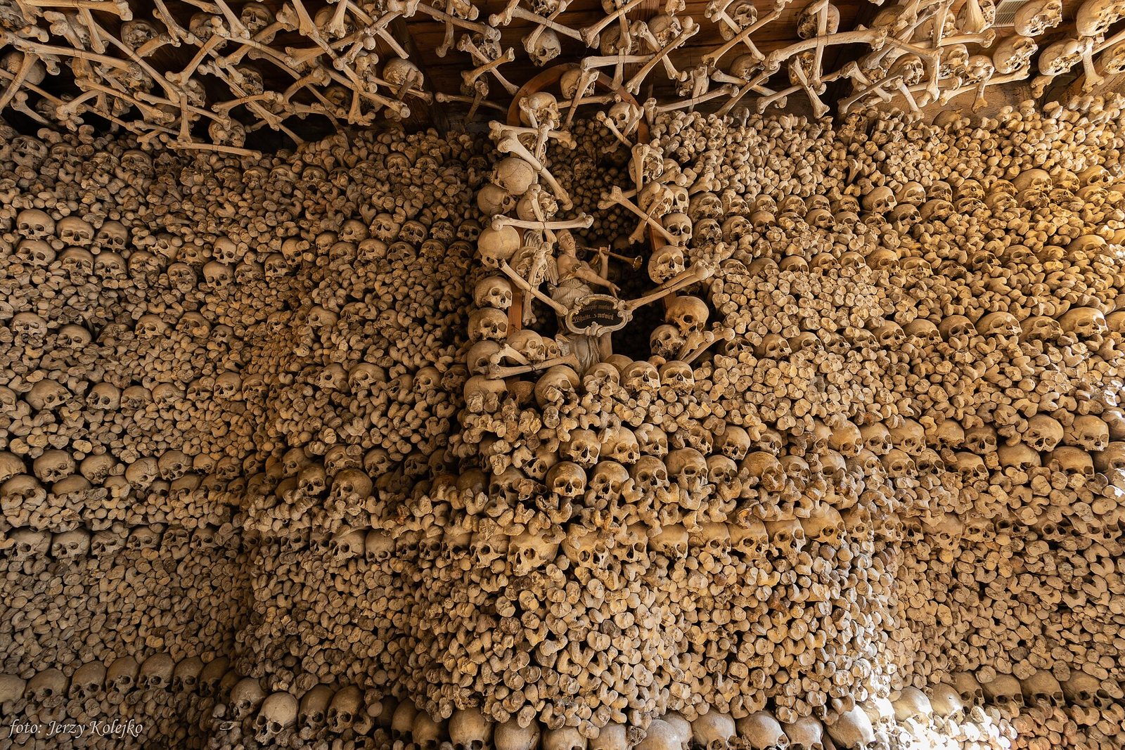 A corner of the chapel interior where the walls are built entirely of rows of skulls, with long bones crossed in patterns along the ceiling above