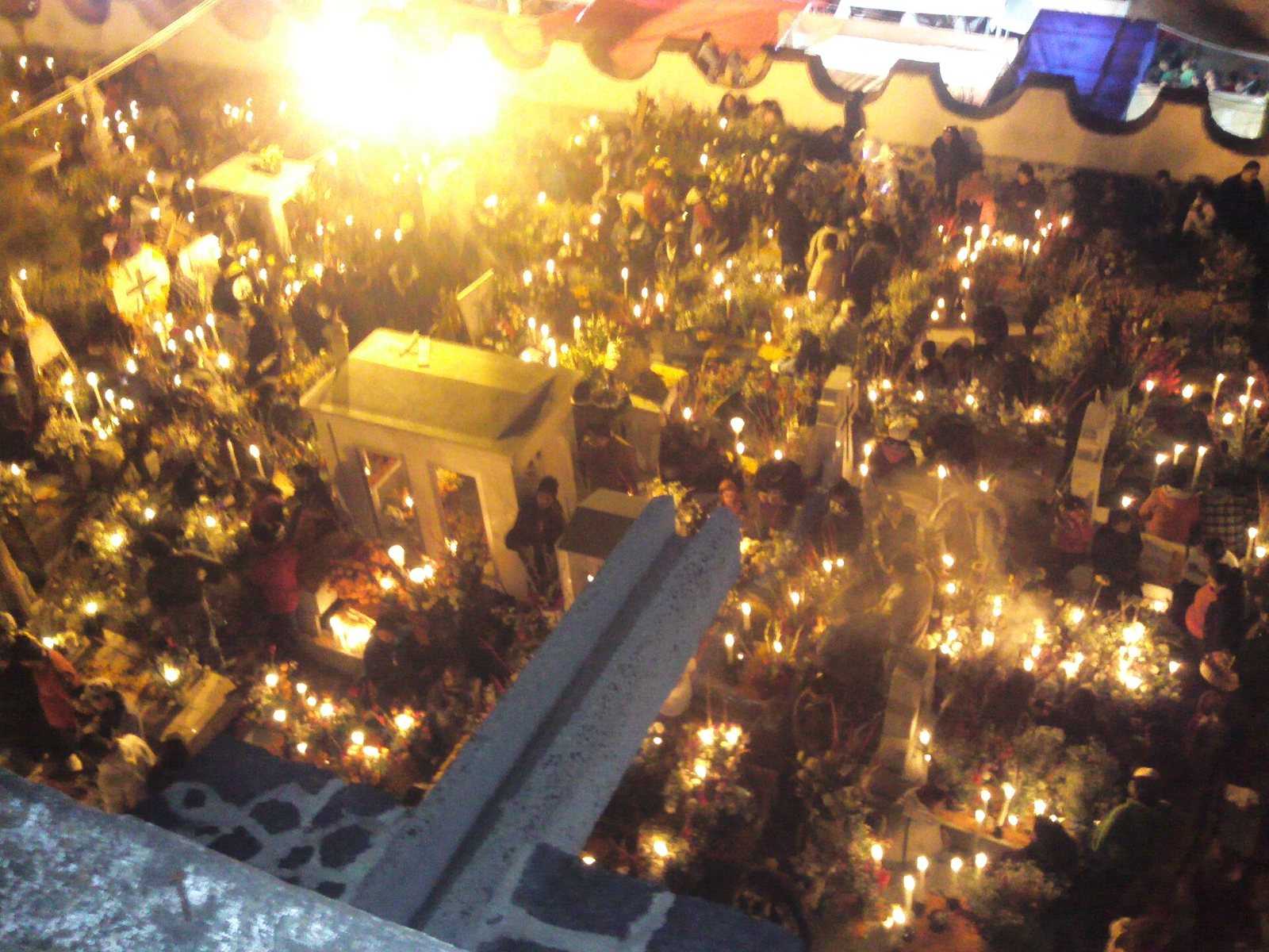 The Mixquic cemetery seen from above at night during the alumbrada, its graves covered in lit candles and flowers among the crowd