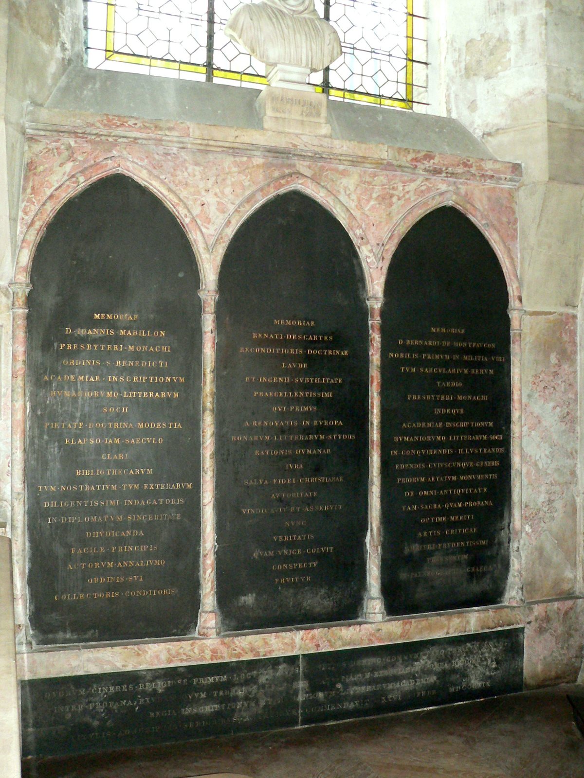 Three dark arched memorial plaques with Latin inscriptions set into a pink-veined stone wall, for Mabillon, Descartes and Montfaucon