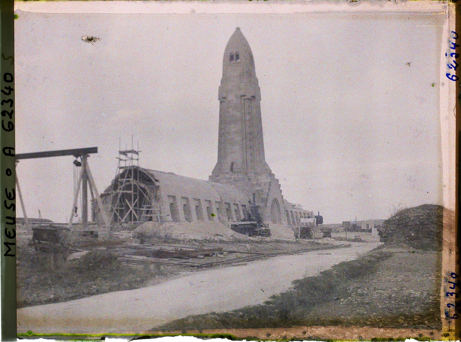 A faded autochrome of the ossuary under construction: the lantern tower already standing, scaffolding on the long vaulted building beside it, a crane at left and an empty road in front
