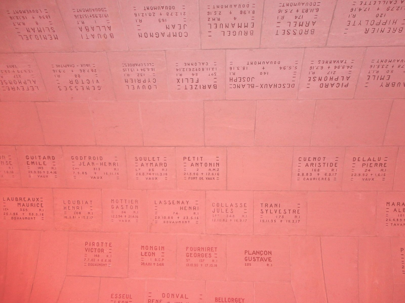Rows of small stone plaques on the vault, each engraved with a soldier's surname, first name and dates, seen in a pinkish light