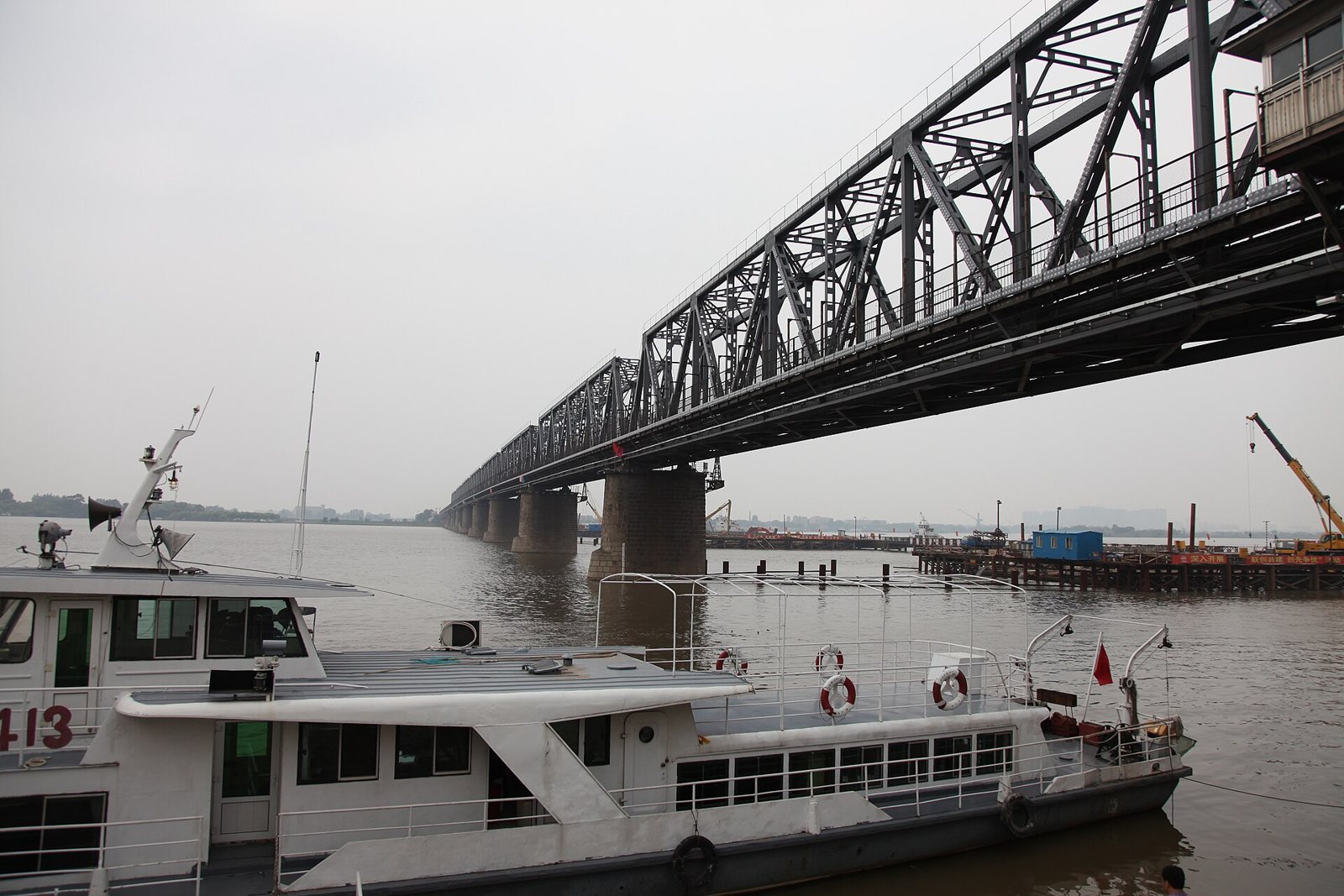 The Old Binzhou Railway Bridge over the Songhua River at Harbin, a long steel truss bridge on stone piers, with a passenger boat moored in the foreground