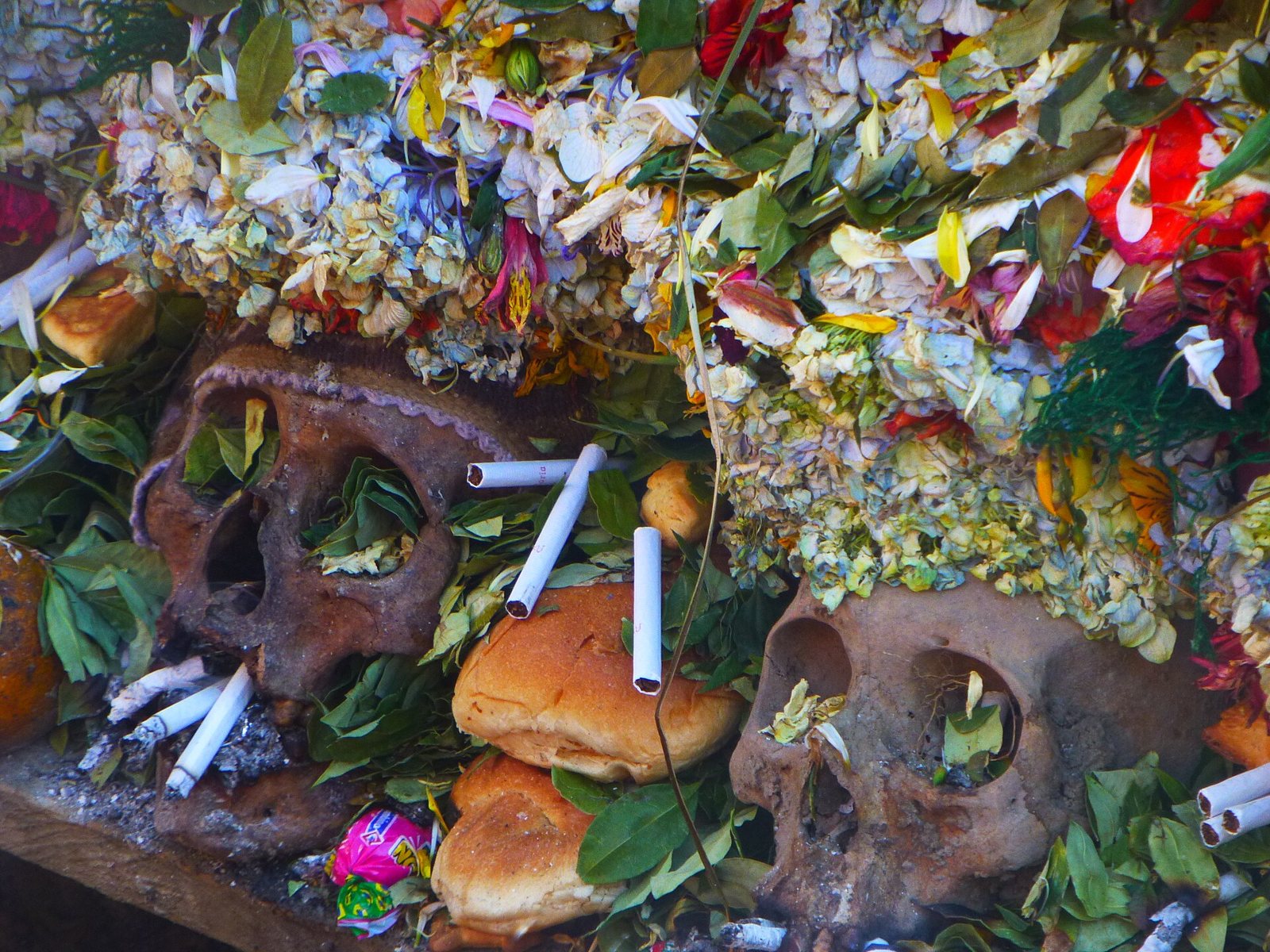 Ñatitas under heaps of fresh flower petals, with bread rolls, coca leaves and lit cigarettes set in front of them