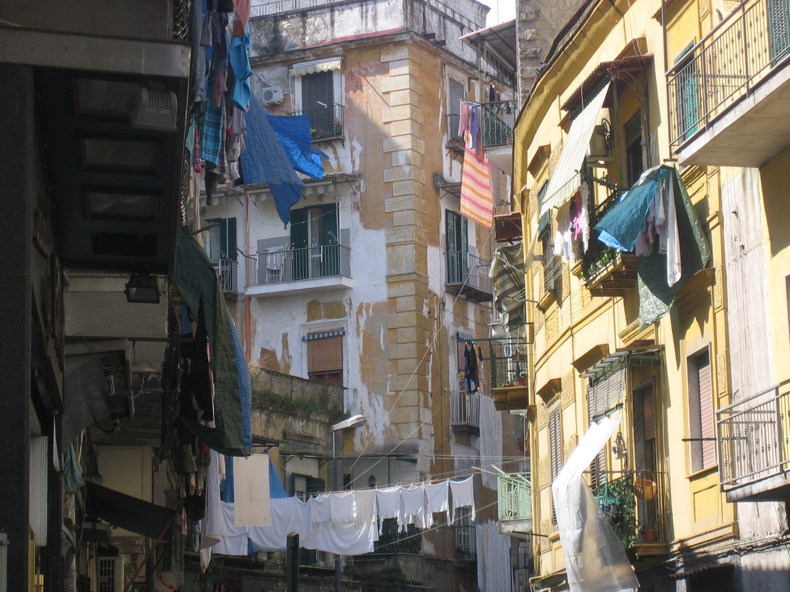 A narrow street in the Rione Sanità in Naples, lined with tall apartment buildings with balconies, shutters and washing hung on lines across the street