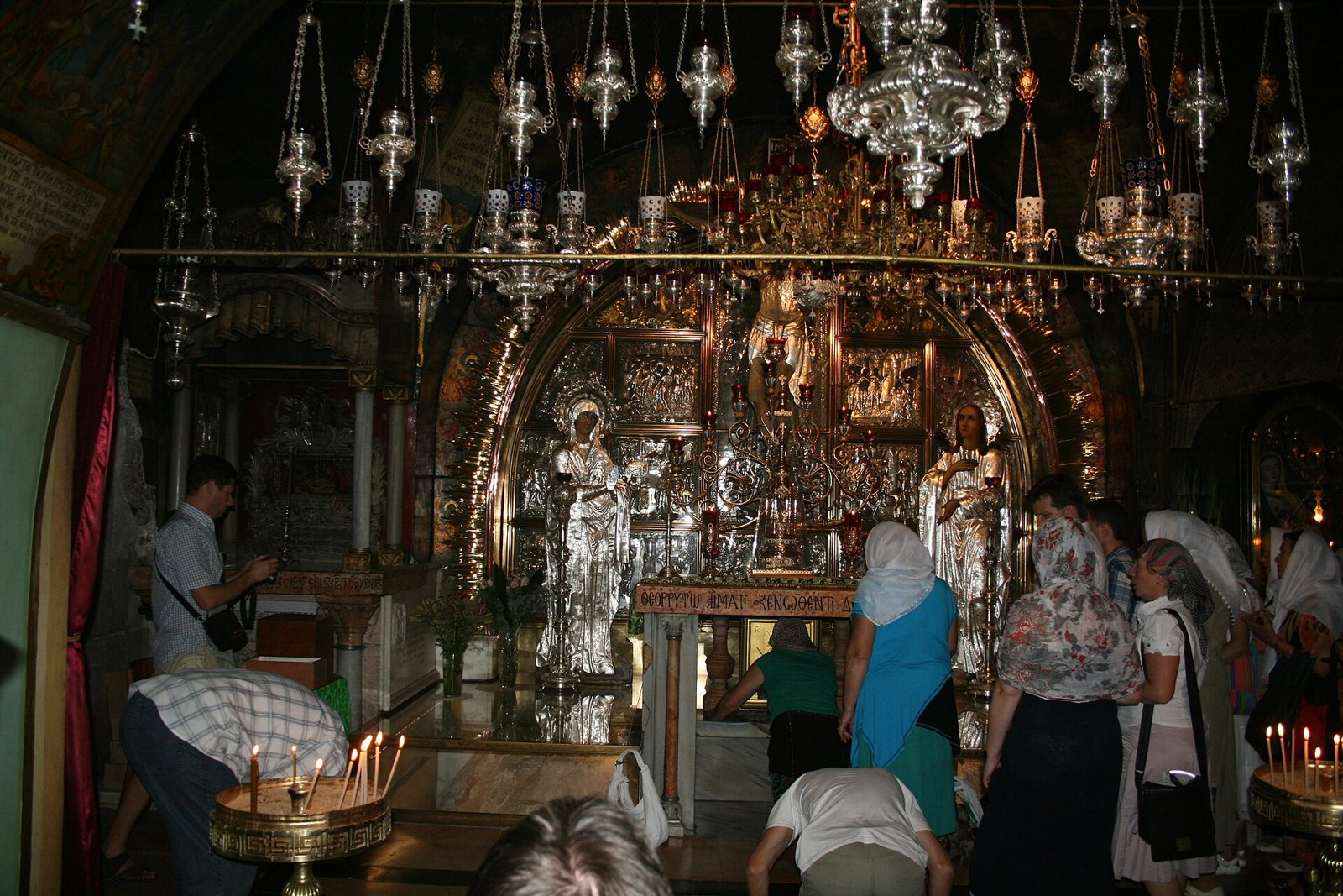 The silver and gold Golgotha altar in the Church of the Holy Sepulchre, hung with many lamps, with pilgrims standing and kneeling before it
