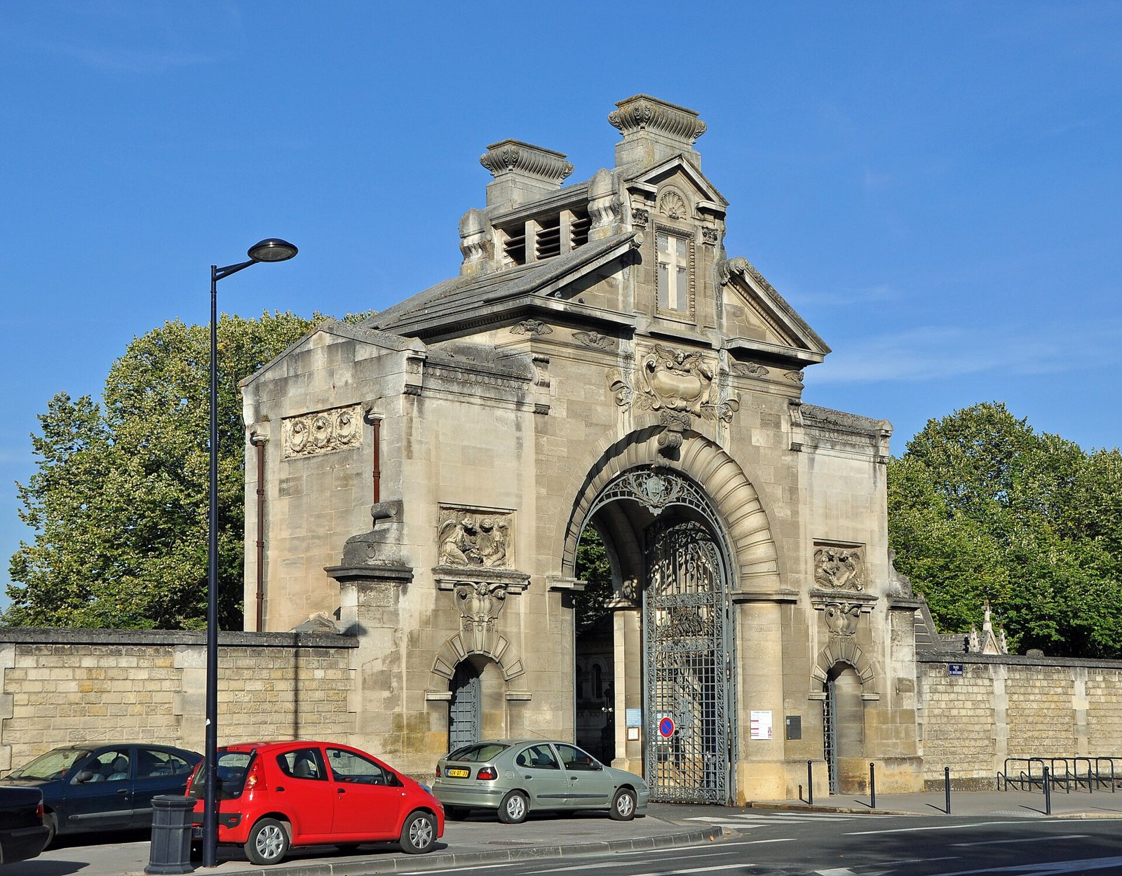 The stone main gate of La Chartreuse cemetery in Bordeaux, with an arched iron gateway, seen from the street