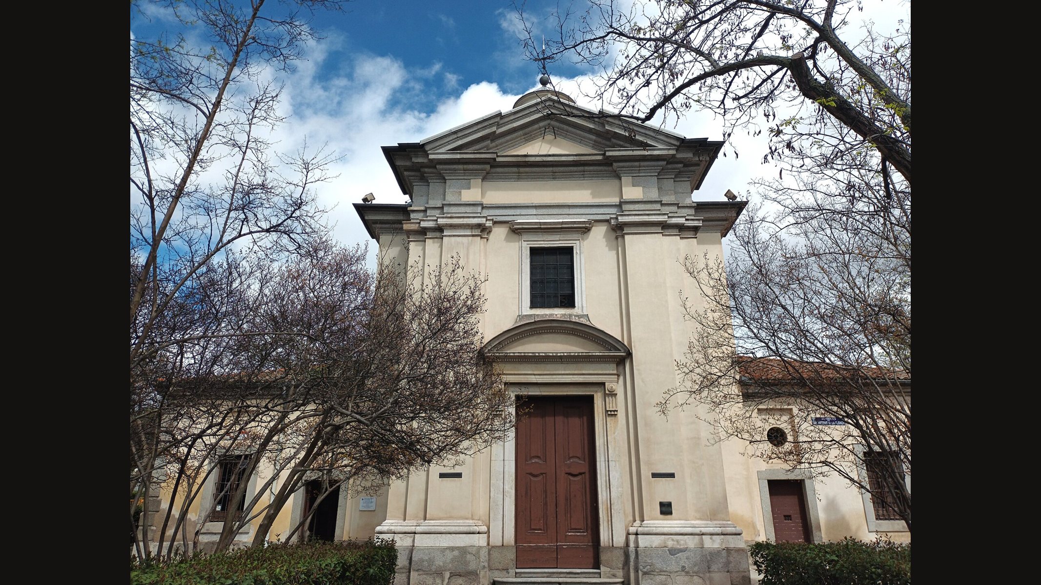 The pale neoclassical front of the Hermitage of San Antonio de la Florida in Madrid, with a pediment and a tall wooden door, framed by bare branches