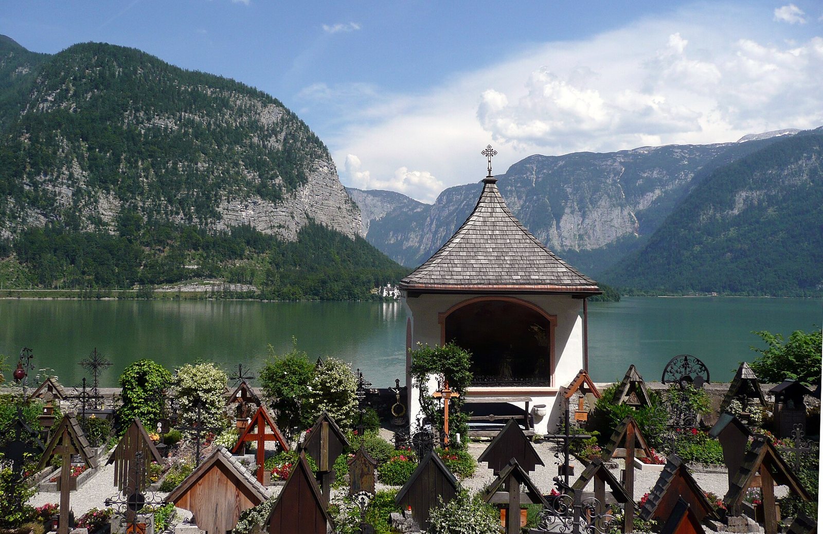 The Hallstatt churchyard, crowded with wooden grave crosses and flowers, beside a small chapel with Lake Hallstatt and steep mountains behind