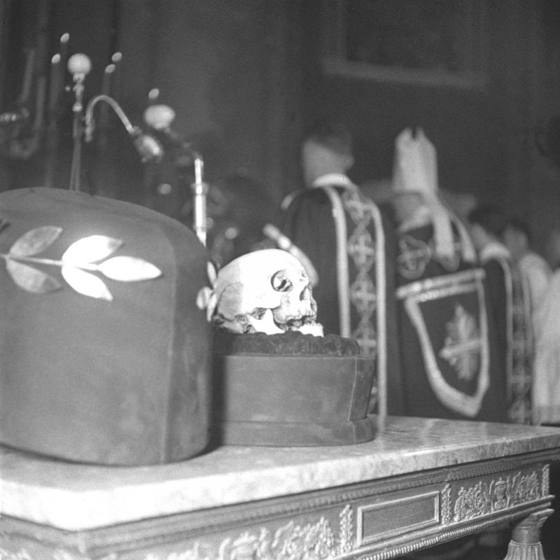 Black-and-white photograph of Haydn's skull resting on a small cushion beside a laurel-decorated casket on an altar table, with clergy in vestments behind