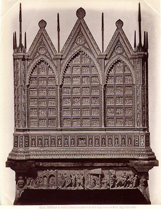 Sepia photograph of a tall carved altarpiece with three pointed Gothic arches, covered in rows of tiny figures, on a dark base