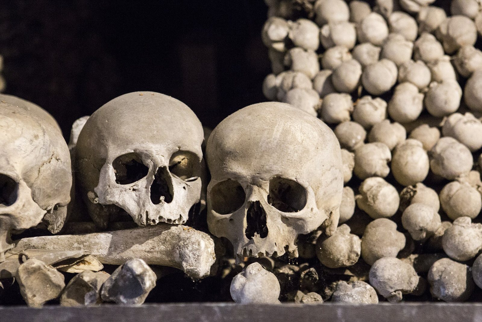 Close view of two weathered skulls resting on long bones inside the Sedlec Ossuary, with a heap of rounded bone ends stacked behind them against a dark background