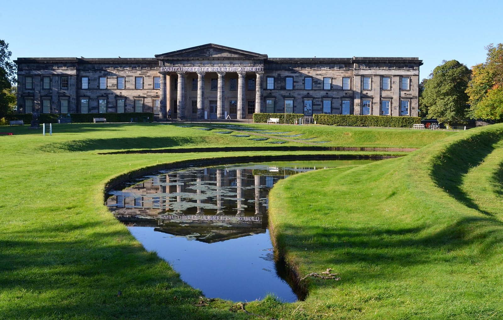 The columned neoclassical stone front of Modern One in Edinburgh, seen across a green lawn and a curved pool