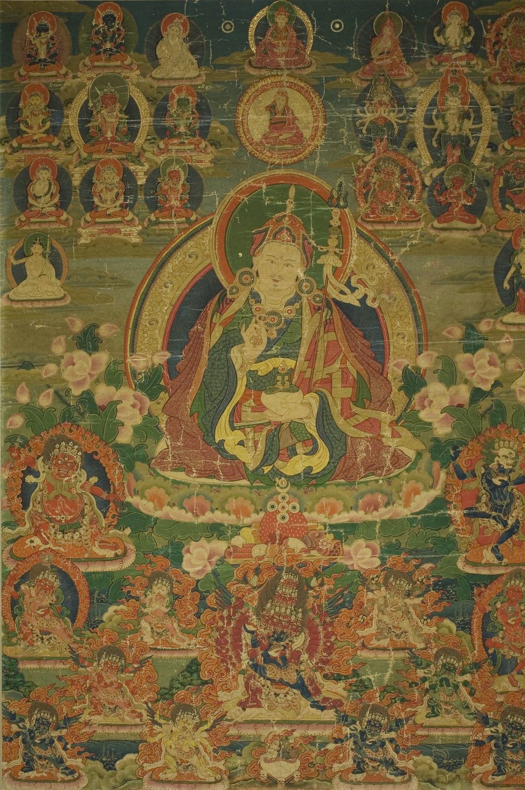 A Tibetan painted banner with Guru Padmasambhava seated at the centre in a halo, holding a skull cup in his lap, with rows of deities above and fierce guardians below