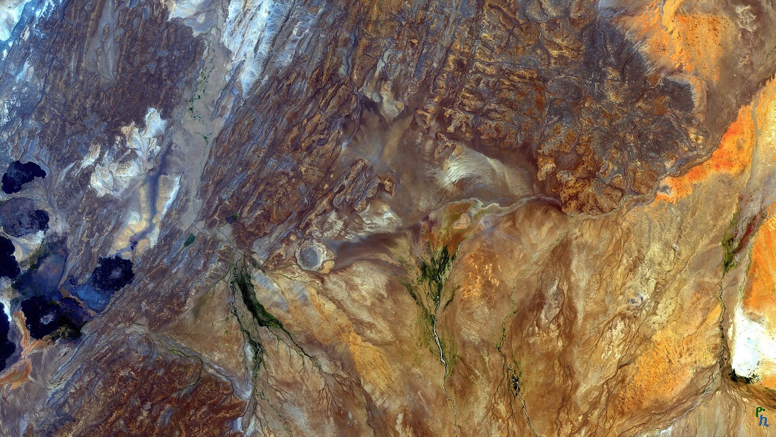 False-colour satellite view of the Afar Triangle in Ethiopia: bands of brown, orange and blue-grey rock, dark crater lakes at the left and green stream lines winding through dry ground
