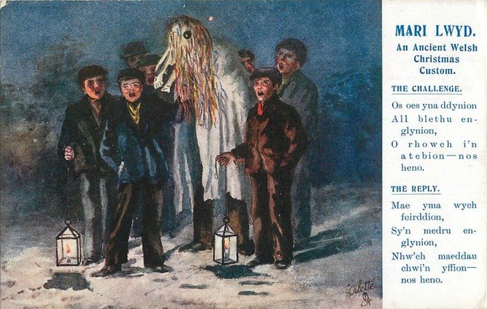 An old colour postcard headed Mari Lwyd, An Ancient Welsh Christmas Custom: a pale sheeted horse figure with streaming ribbons among a group of boys and men with two lanterns, beside printed Welsh verses for the challenge and the reply