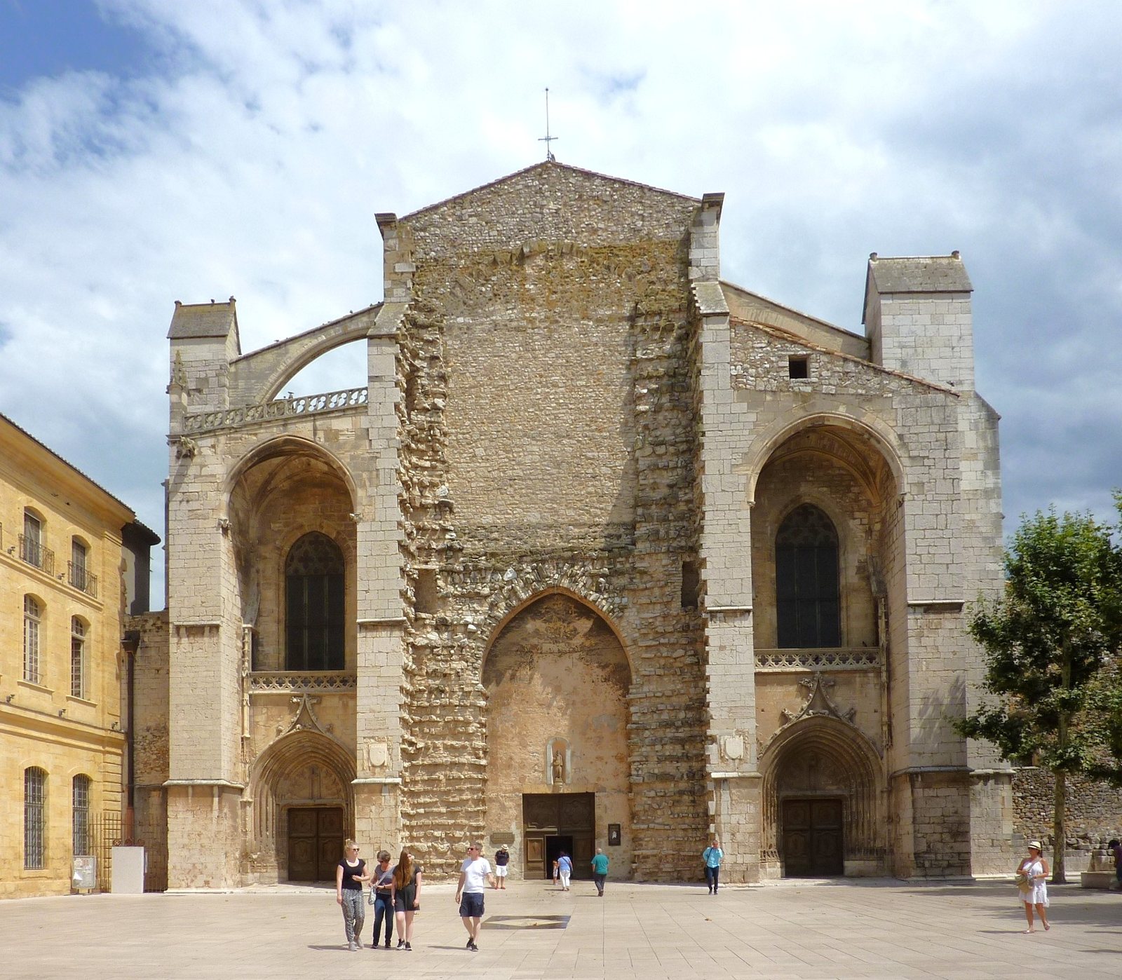 The unfinished west front of the Basilica of Sainte-Marie-Madeleine at Saint-Maximin, a tall pale stone facade with three doorways, seen across an open square