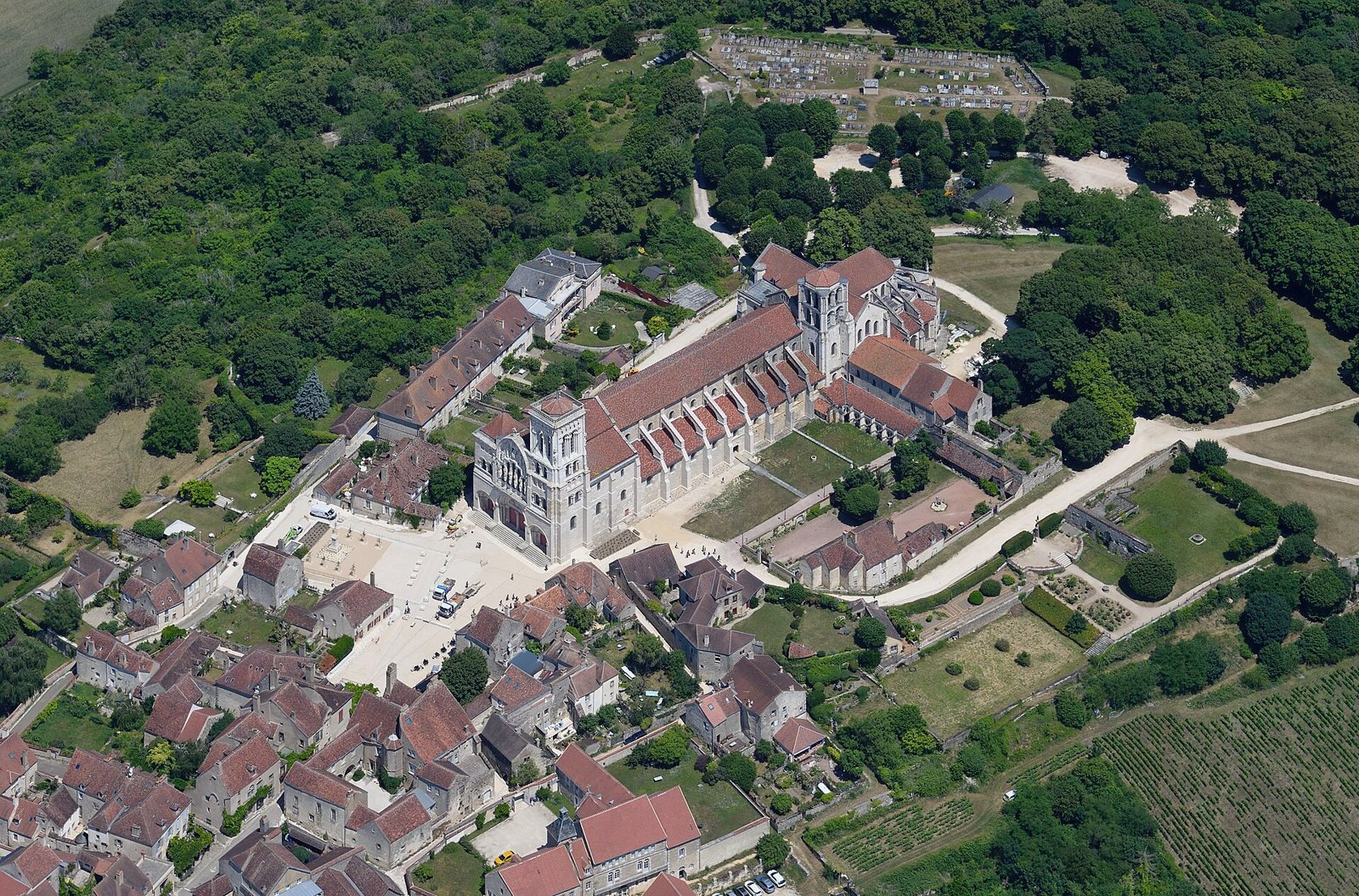 Aerial view of the hilltop town of Vézelay, with the long roof of the Basilica of Sainte-Marie-Madeleine at its centre among red-roofed houses and woods
