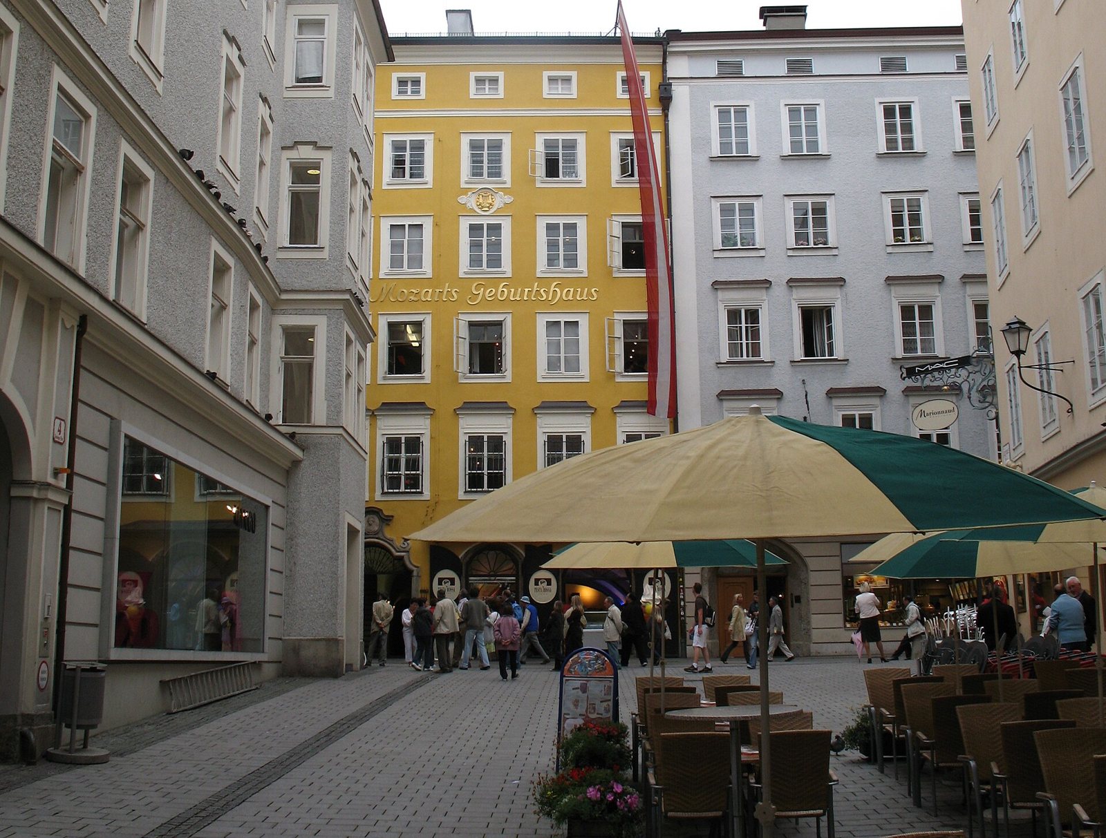 The tall yellow facade of Mozart's Birthplace, lettered Mozarts Geburtshaus, above a small square with café umbrellas and visitors