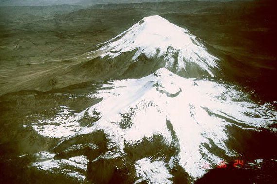 Aerial view of two snow-covered volcanic cones, Nevado Ampato and the active Sabancaya, seen from the northeast over dark mountain slopes