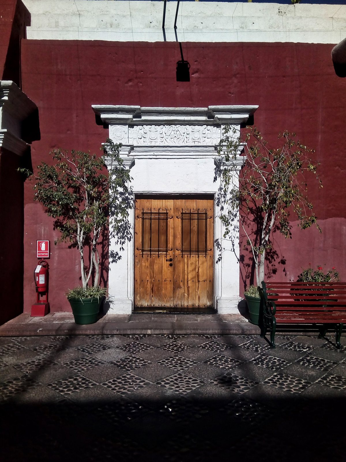 The carved white stone doorway and wooden double door of the Museo Santuarios Andinos in Arequipa, set in a deep red wall with a paved courtyard in front