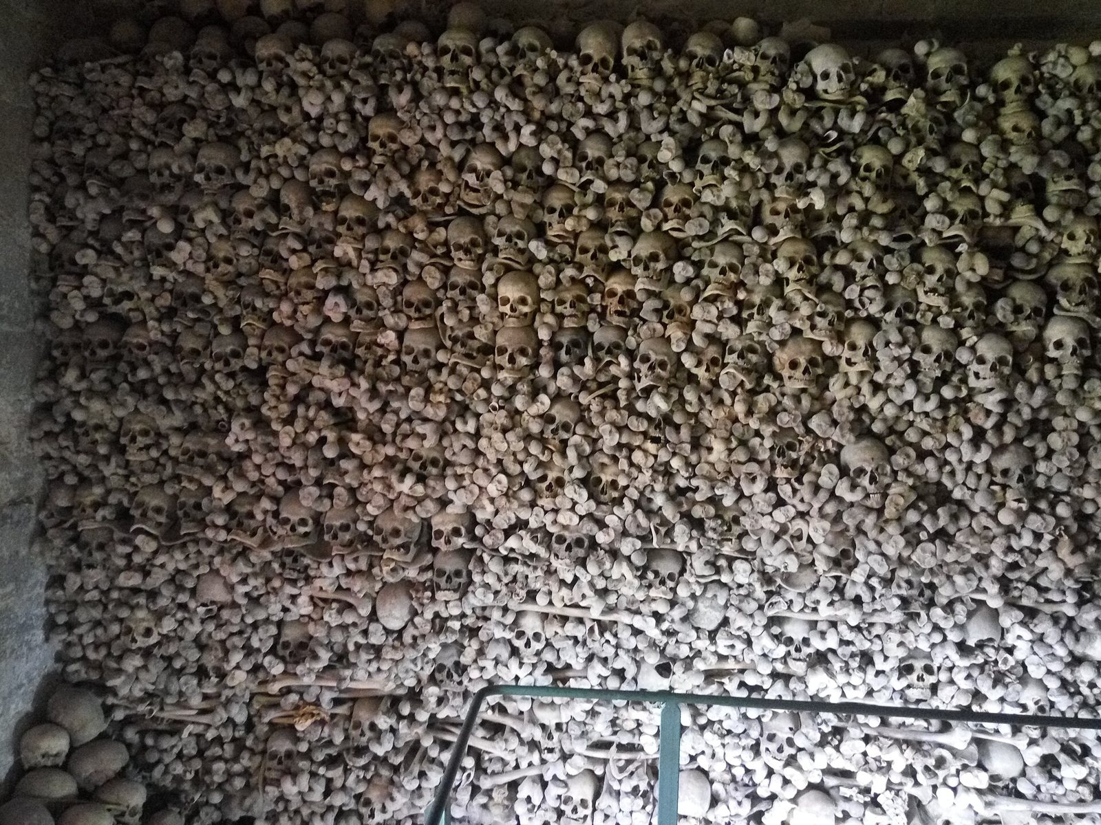 A wall of the ossuary in the church of Santa María in Wamba, stacked with skulls and long bones behind a low metal rail