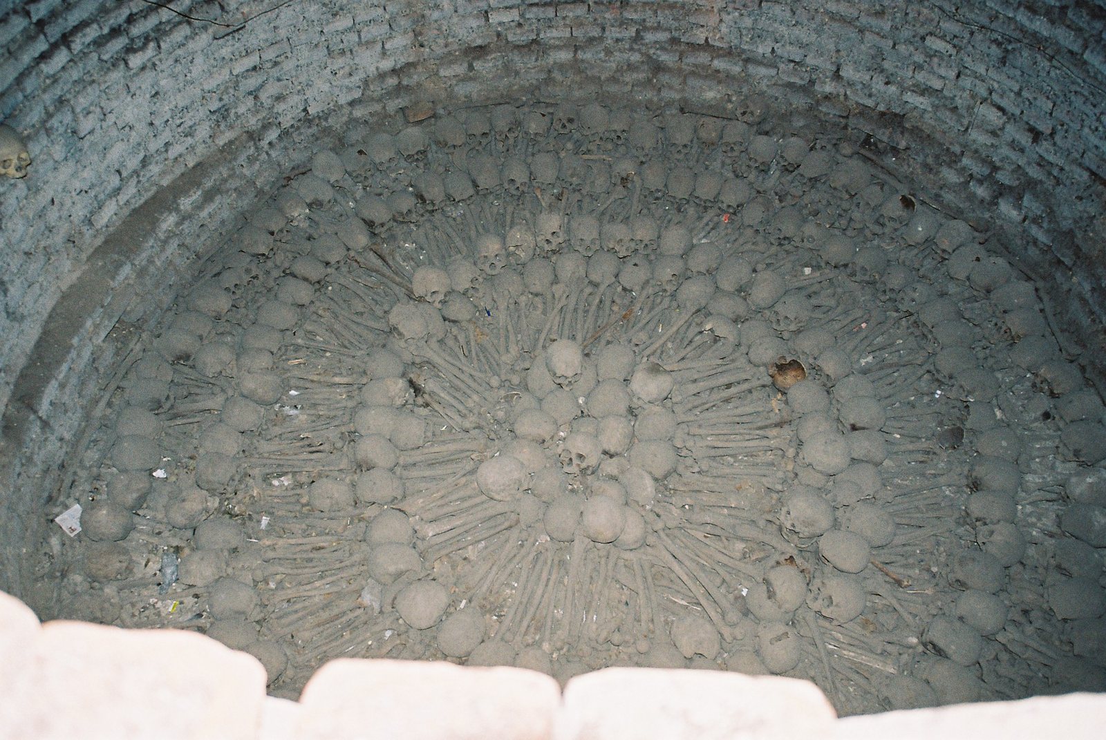 Looking down into a round brick pit in the Lima catacombs, where skulls and long bones are laid in concentric rings and a starburst pattern