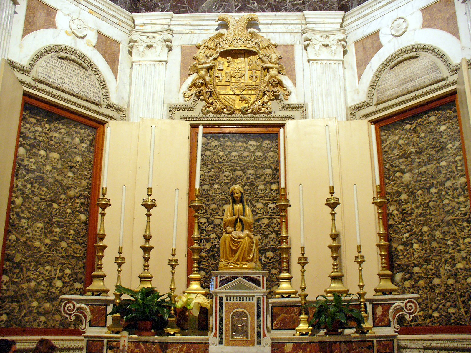 The altar of the Chapel of the Martyrs in Otranto Cathedral, with a gilded statue at the centre and large wall cabinets filled with skulls on either side