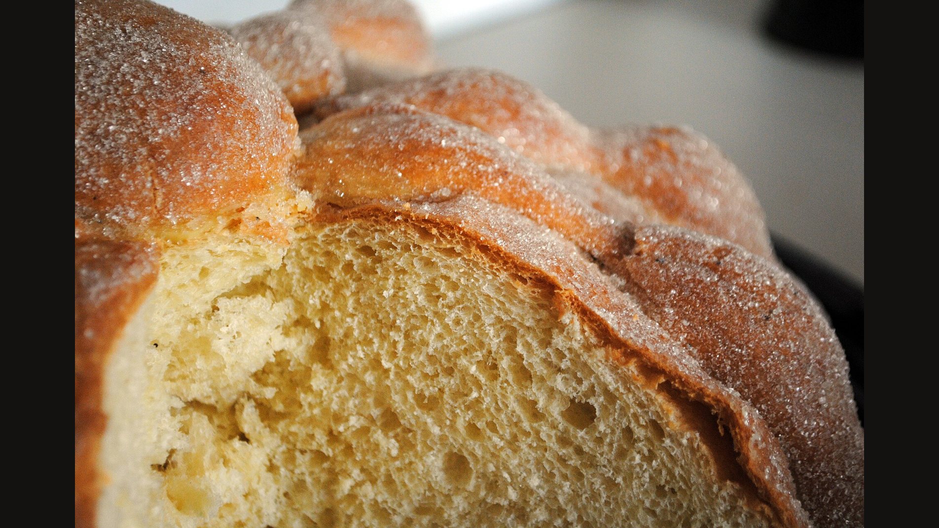Close view of a cut pan de muerto: a soft yellow crumb under a sugar-crusted top with raised strips of dough