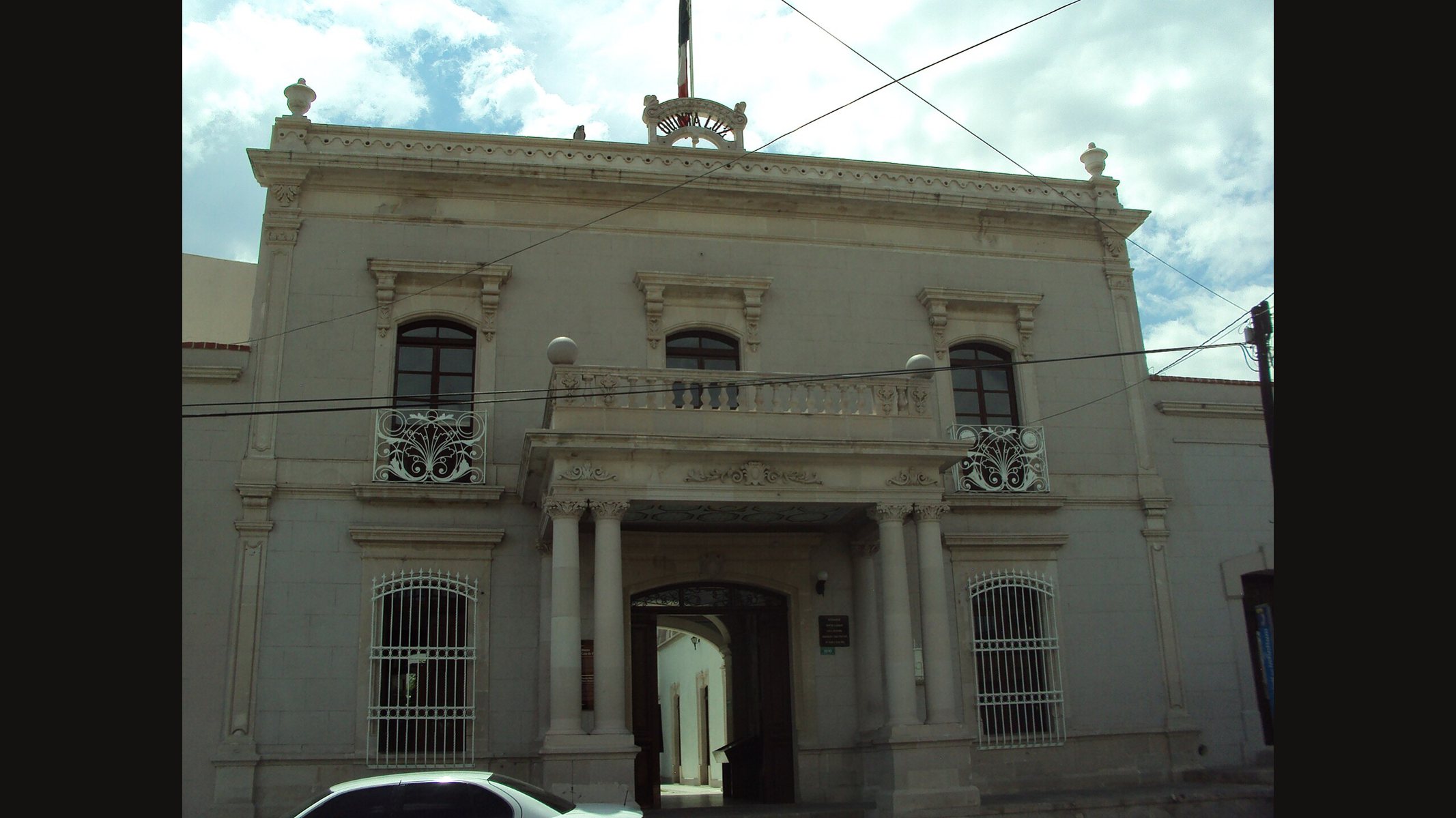 The two-storey front of the Quinta Luz in Chihuahua City, a grey house with a balcony above a columned entrance and barred windows