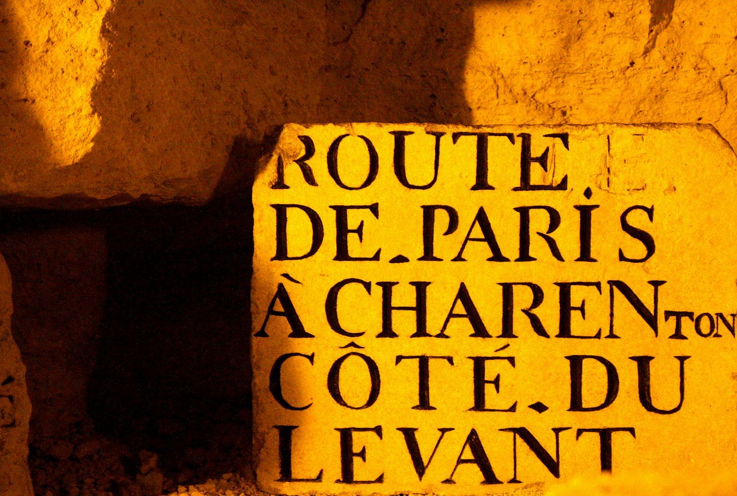 A carved stone plate lit in orange inside the old Paris quarries, reading Route de Paris à Charenton, côté du Levant