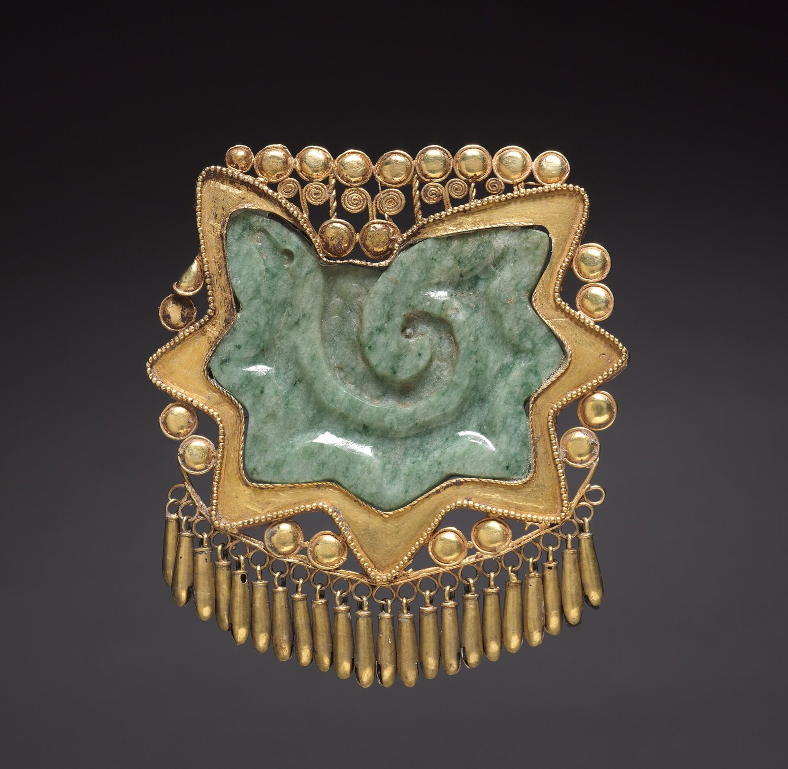 A pectoral ornament of gold and green jade: a carved spiral inside a star-shaped gold frame, with beaded gold edges and a fringe of small gold bells below