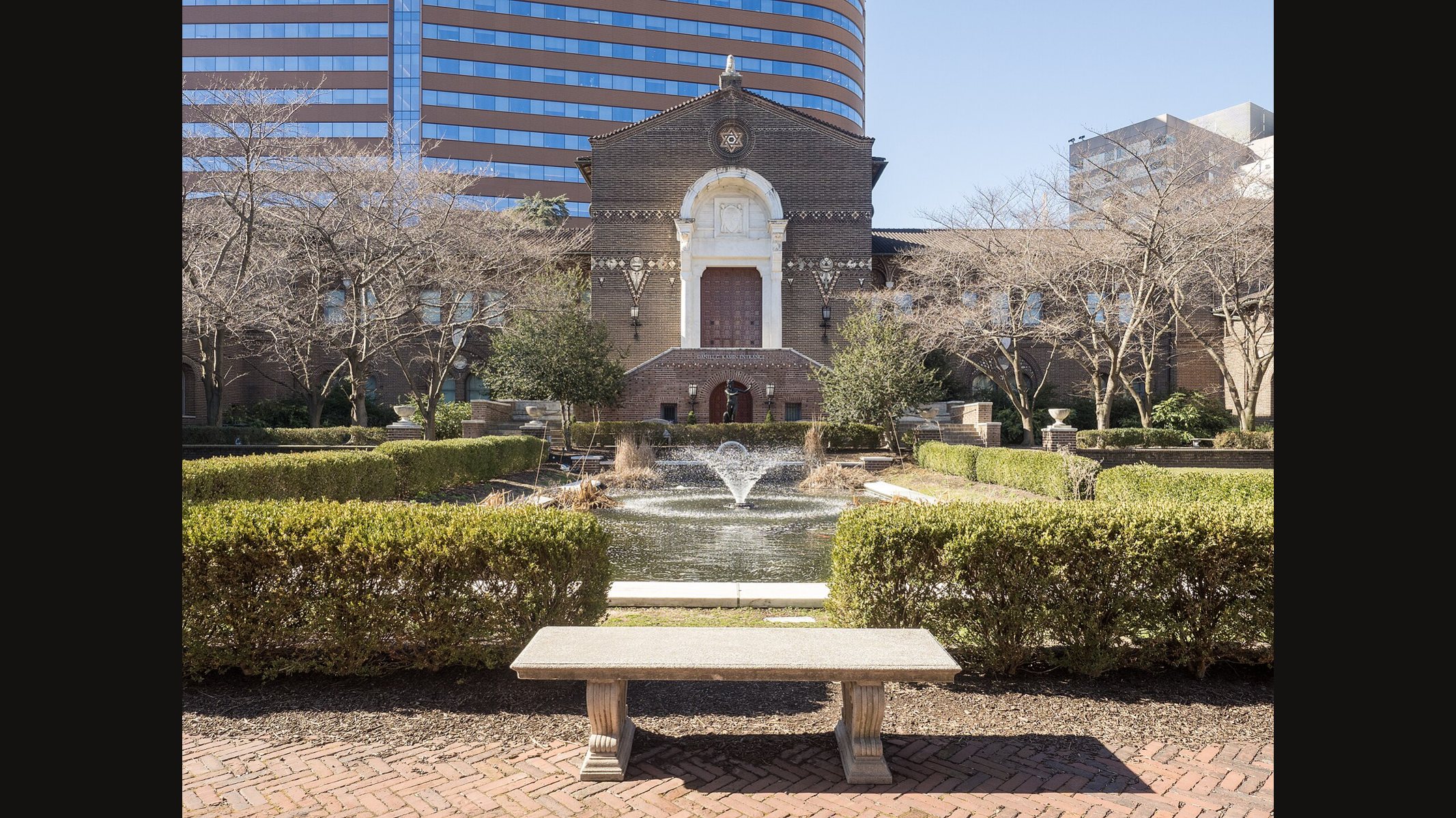 El edificio de ladrillo rojo del Museo Penn en Filadelfia, visto a través de un jardín formal con setos recortados, una pequeña fuente y un banco de piedra