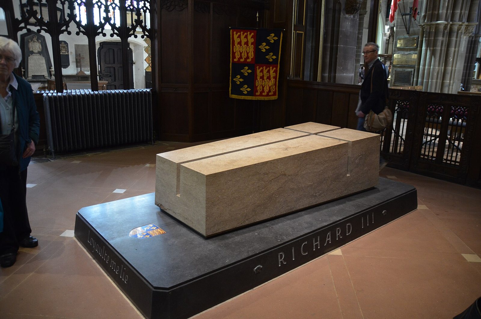 The tomb of Richard III in Leicester Cathedral: a plain pale limestone slab on a dark plinth lettered Richard III, with a coat of arms and wooden screens behind