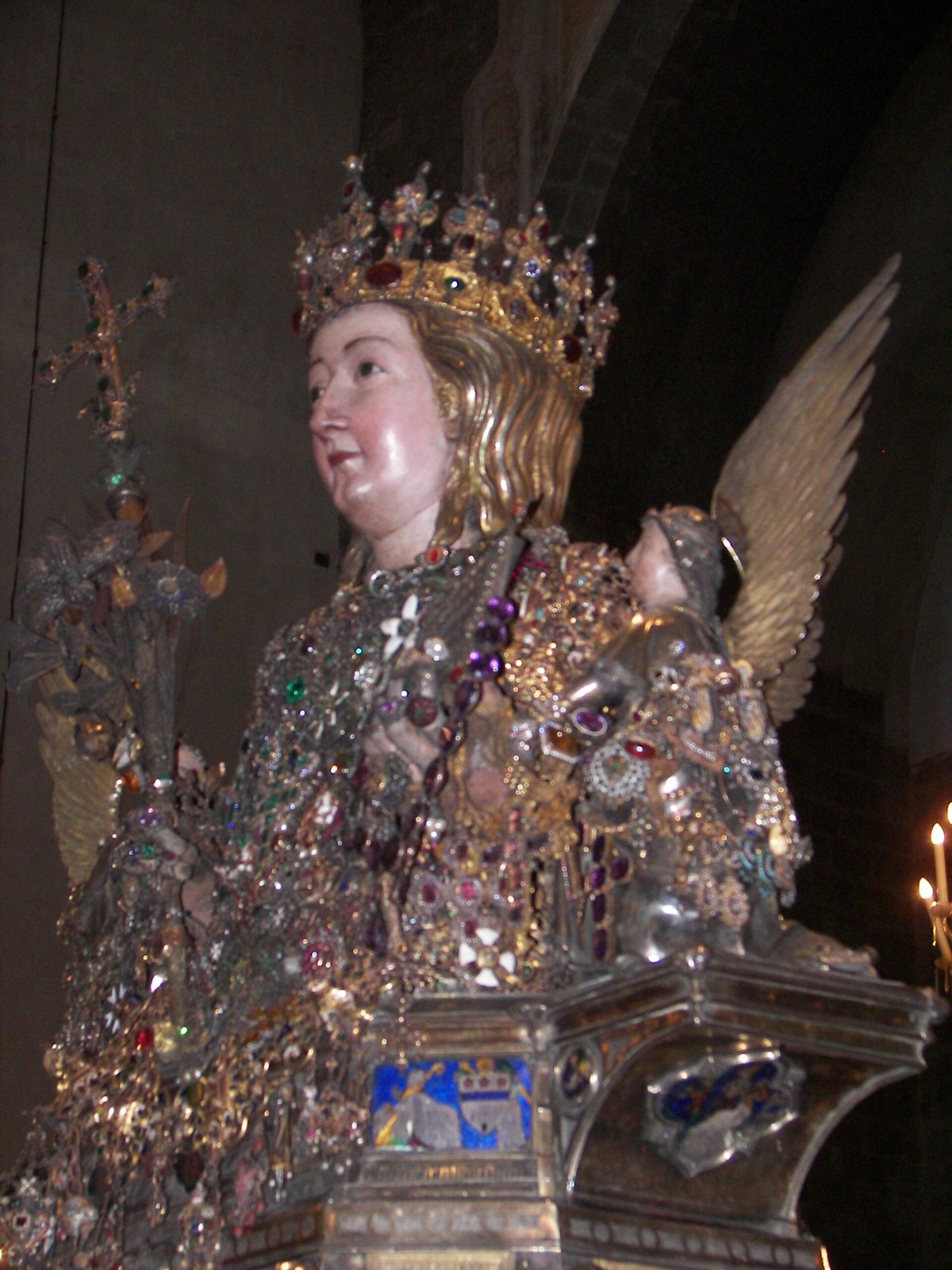 The silver reliquary bust of Saint Agatha in Catania Cathedral, shown from the side: a crowned head, a chest covered in jewels and gold ornaments, an angel's wing and a tall cross behind
