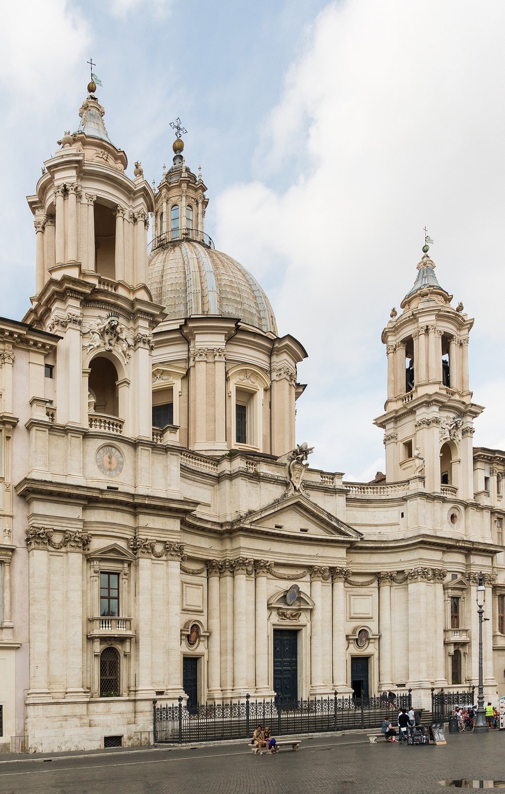 The cream-coloured baroque facade of Sant'Agnese in Agone in Rome, with a central dome, two bell towers and an iron railing along the front