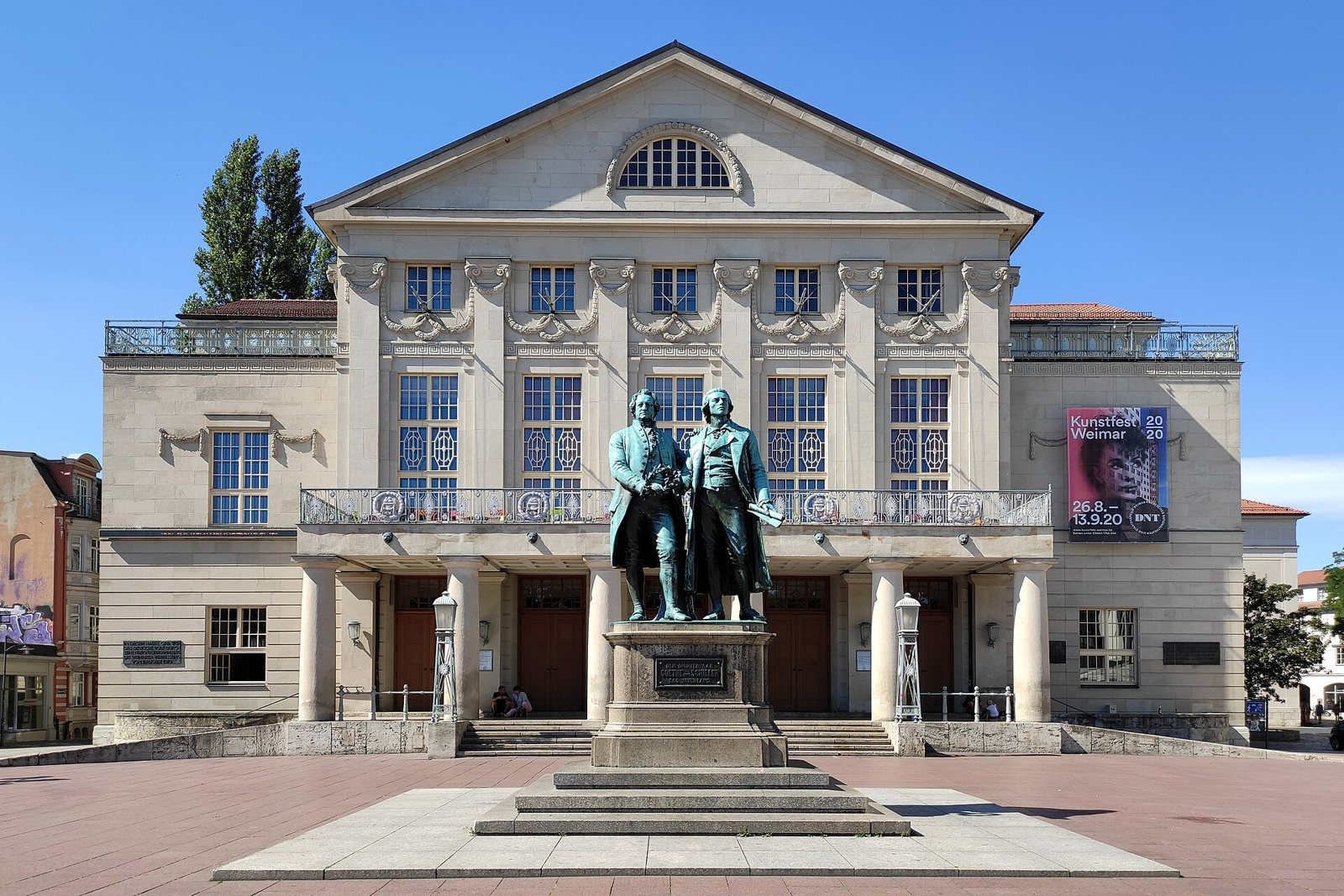 The bronze Goethe and Schiller monument standing side by side on a stone plinth in front of the columned facade of the German National Theatre in Weimar