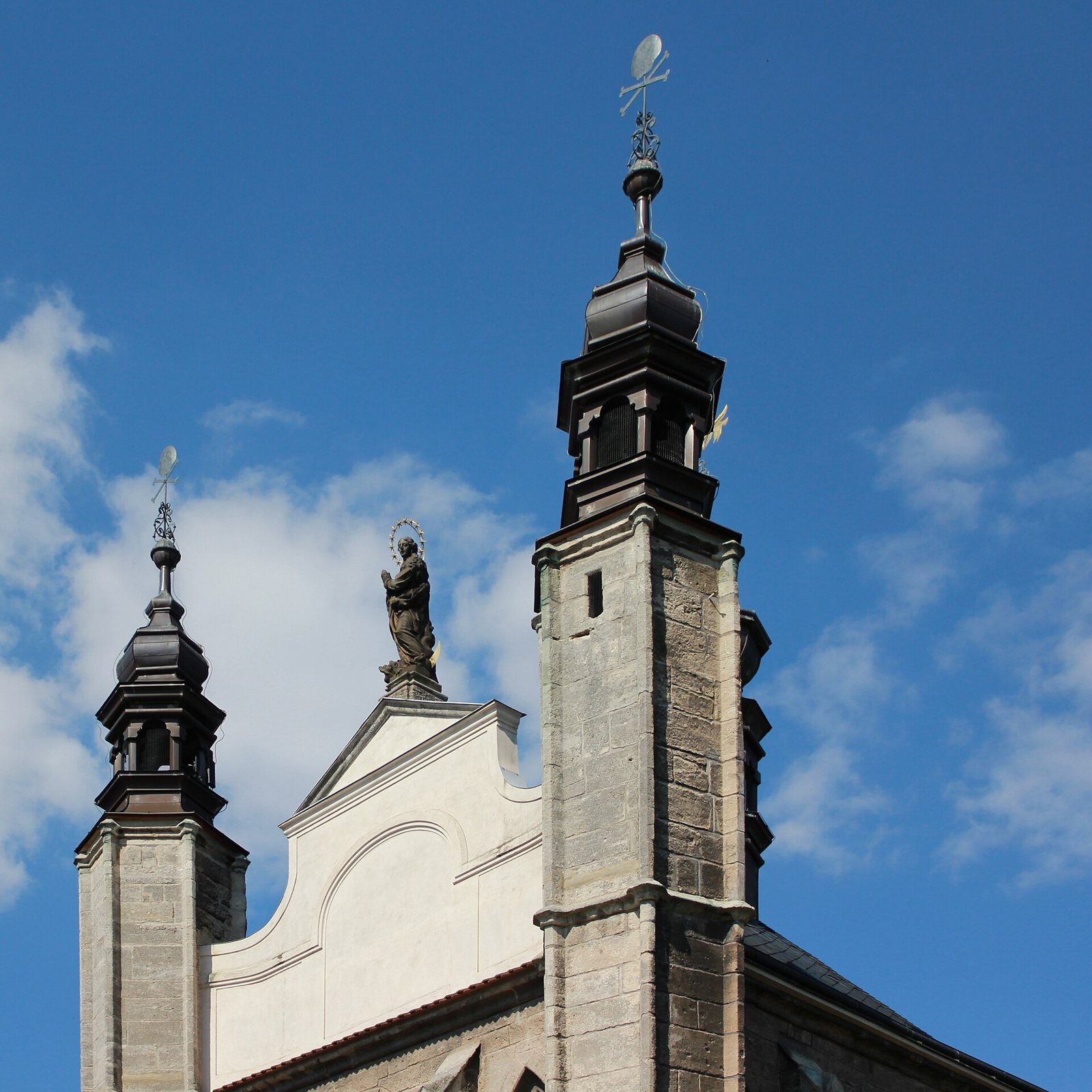 The twin towers and white gable of the Cemetery Church of All Saints in Sedlec against a blue sky with clouds