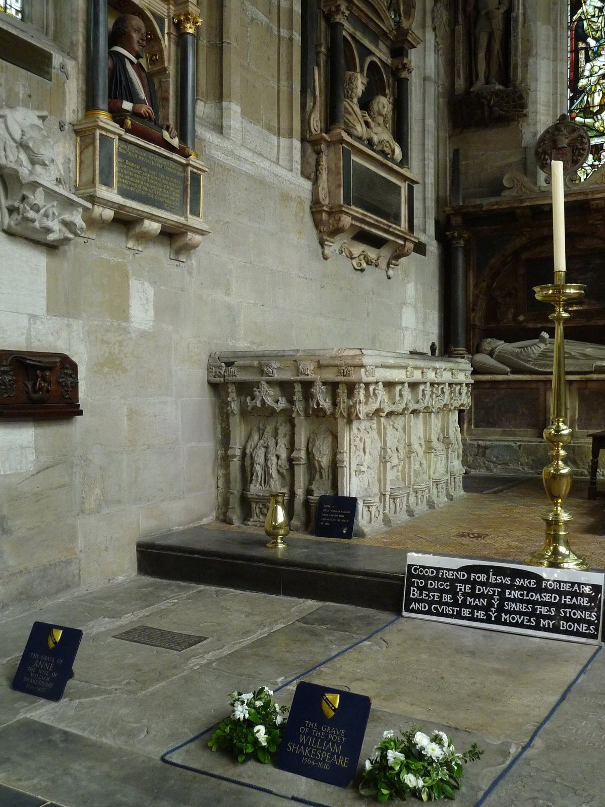The wall monument with Shakespeare's bust above the carved tomb chest and the grave stone with a plaque in the floor, beside a tall candlestick