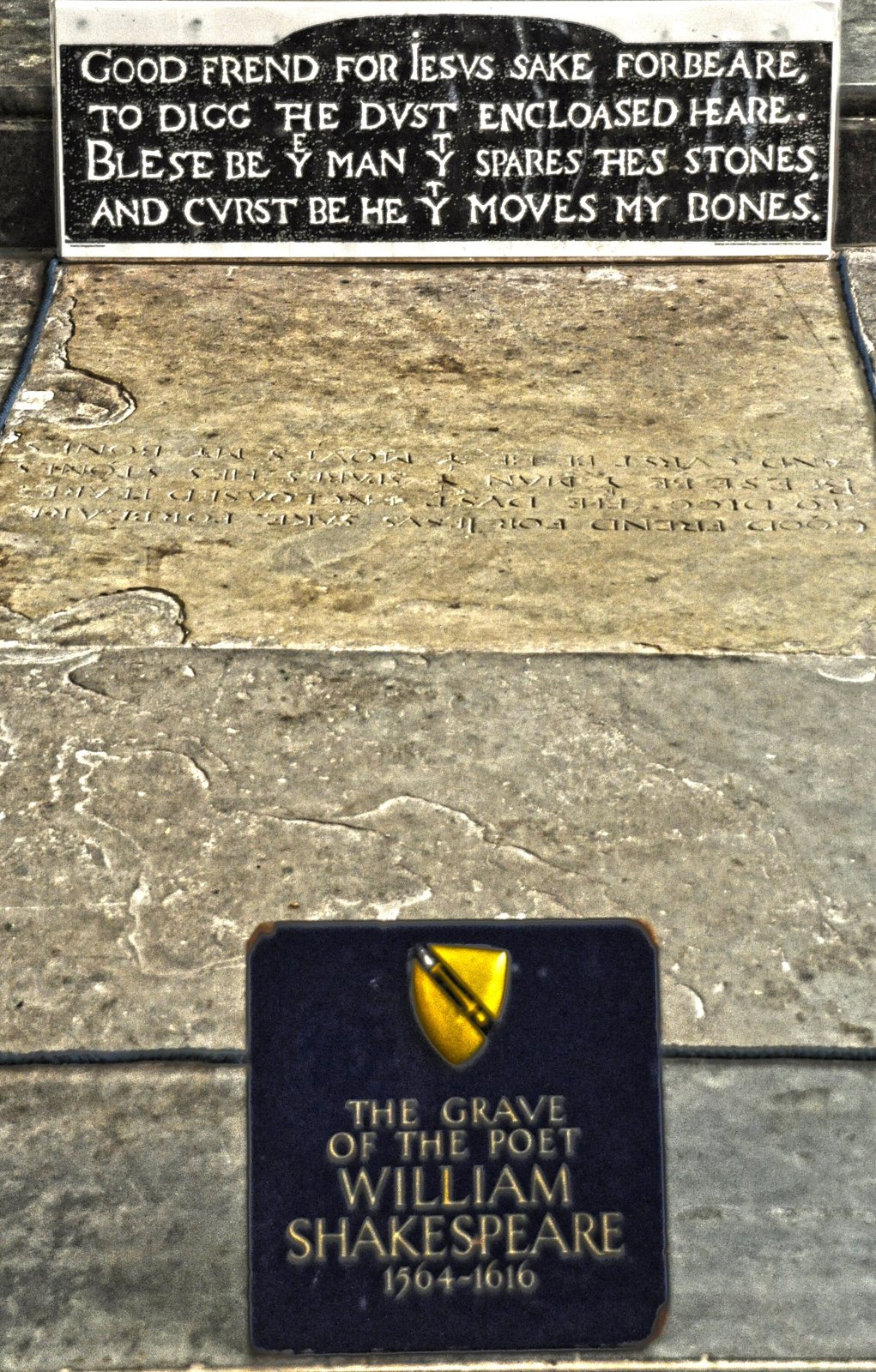 A sign bearing the four lines of the verse "Good frend for Iesvs sake forbeare", above the worn grave stone and a small plaque reading The Grave of the Poet William Shakespeare, 1564-1616