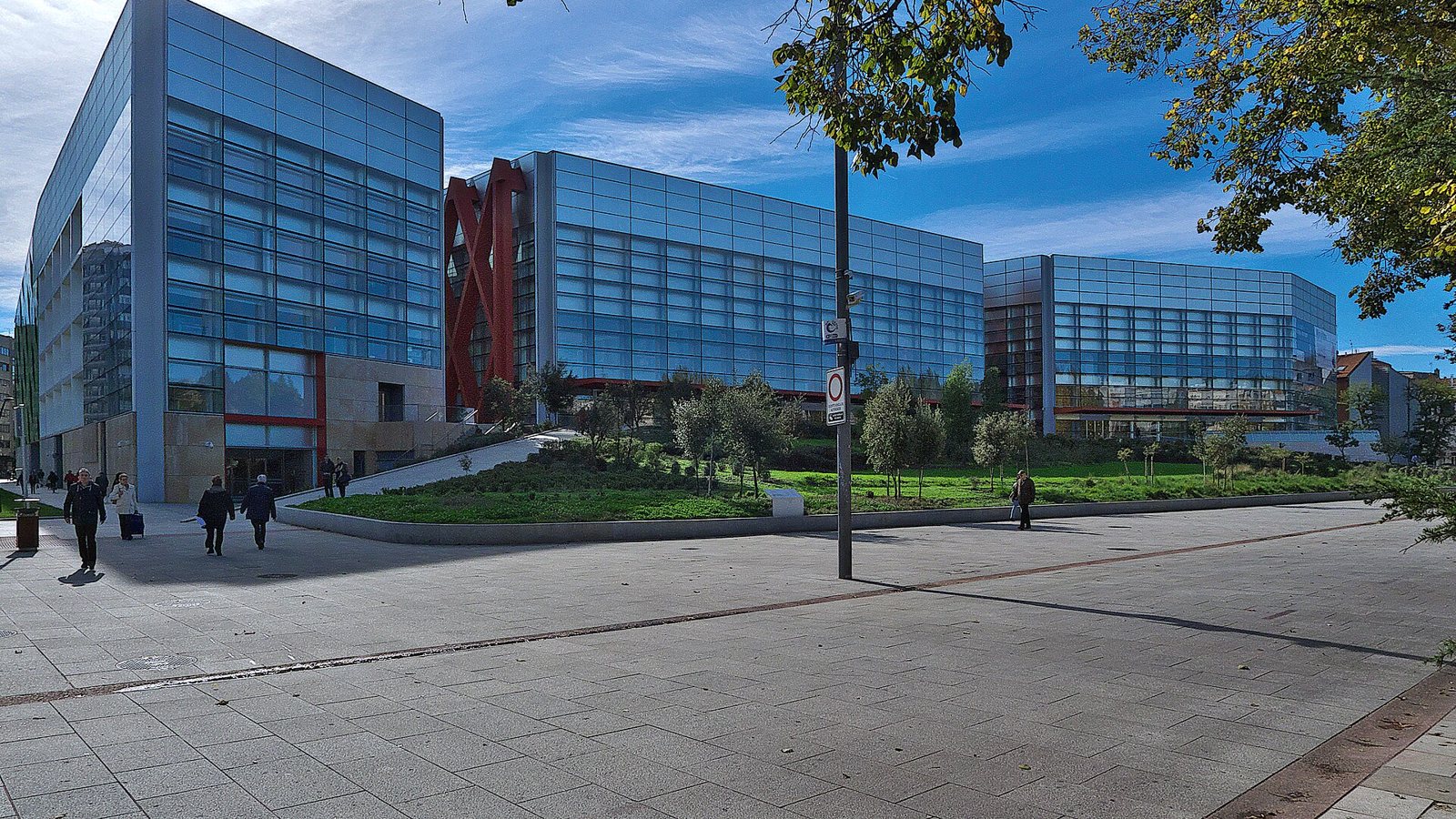 Glass-fronted buildings of the Museo de la Evolución Humana and the human evolution research centre in Burgos, seen across a paved plaza under a blue sky