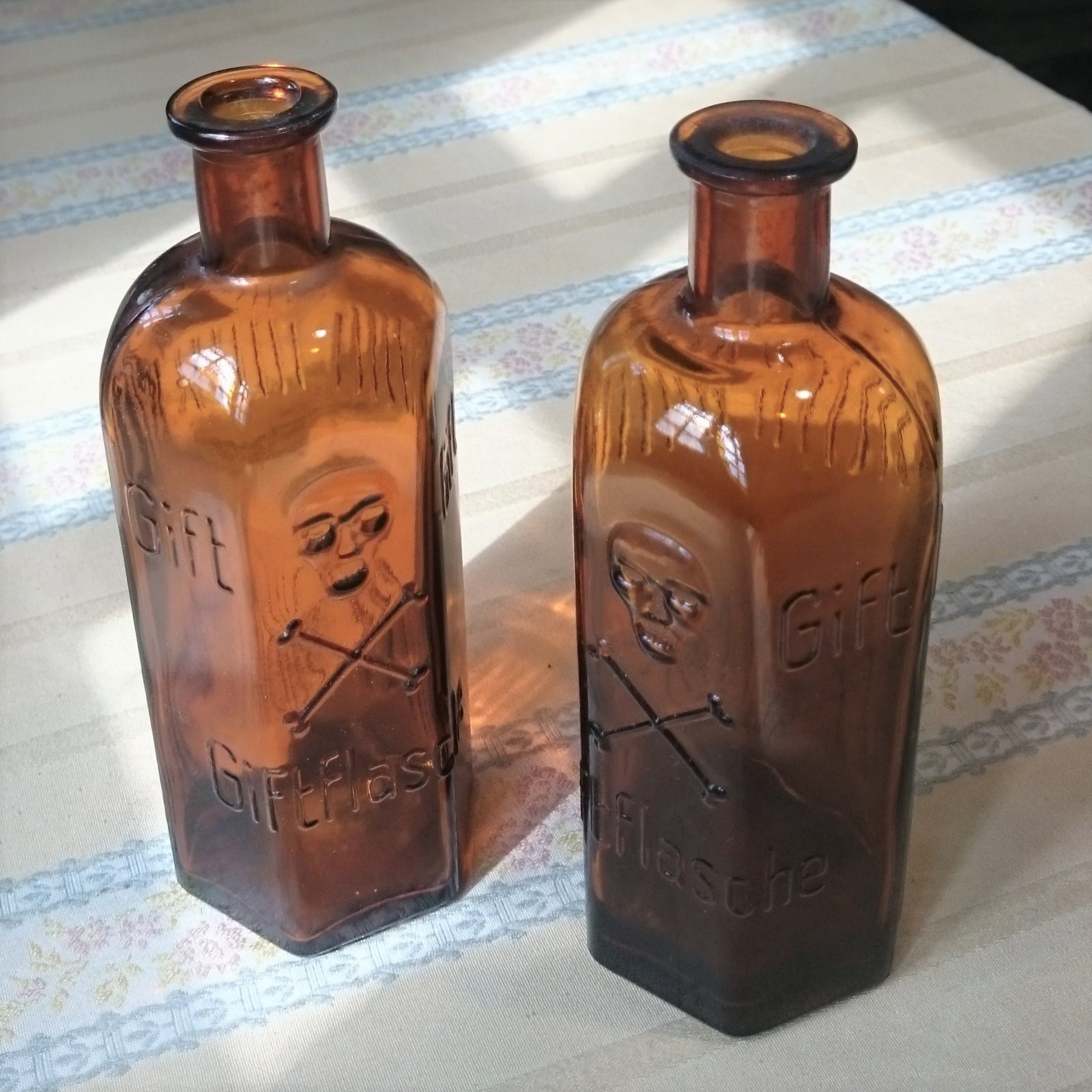 Two amber glass bottles with six sides, each with a raised skull and crossbones and the German words Gift and Giftflasche moulded into the glass